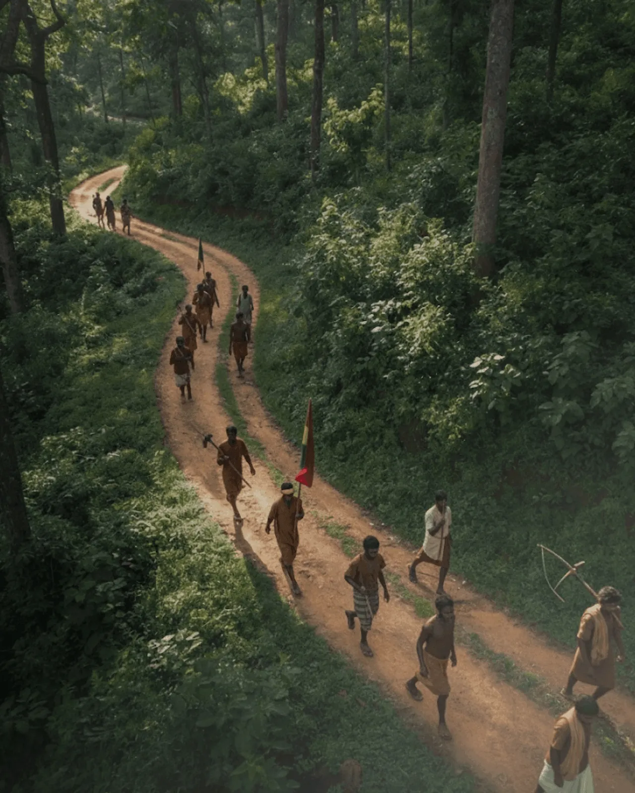 Indigenous men and women of the Chotanagpur Plateau, carrying bows, arrows and battle axes and a tribal flag, walking a forest trail into the Dalma hills during Bishnu Sendra Parv