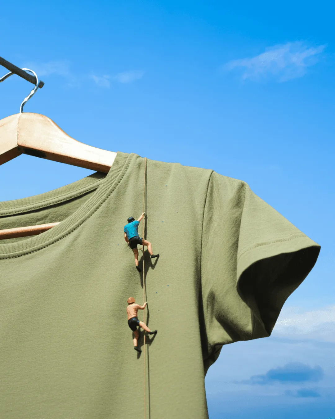 एक हैंगर पर टंगी टी-शर्ट, जिस पर दो छोटे पर्वतारोही चढ़ रहे हैं — 'Clothes Have No Gender' के लिए एक चित्रण