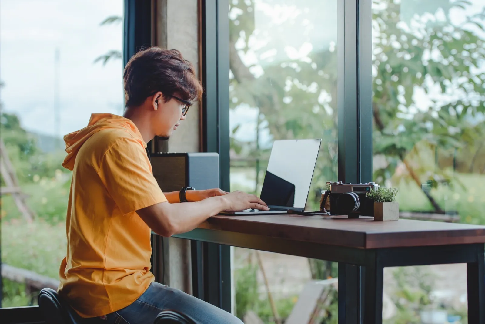 A software engineer coding on a laptop by a window