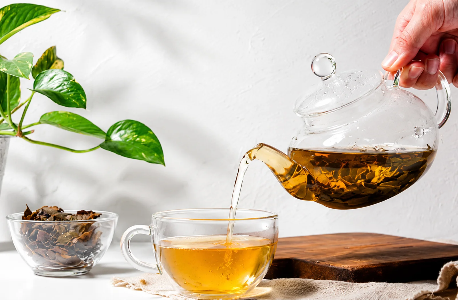 Darjeeling tea being poured from a glass teapot into a glass cup beside a bowl of dried leaves