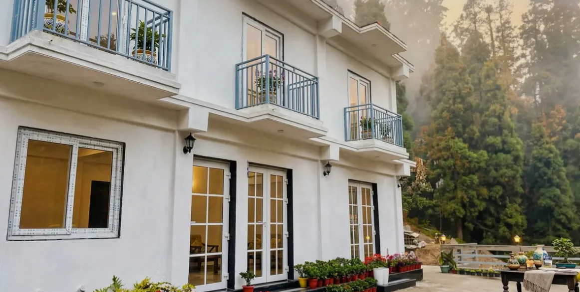 Kulam Homestay: the white two-storey homestay with blue balconies and potted flowers, pine forest behind