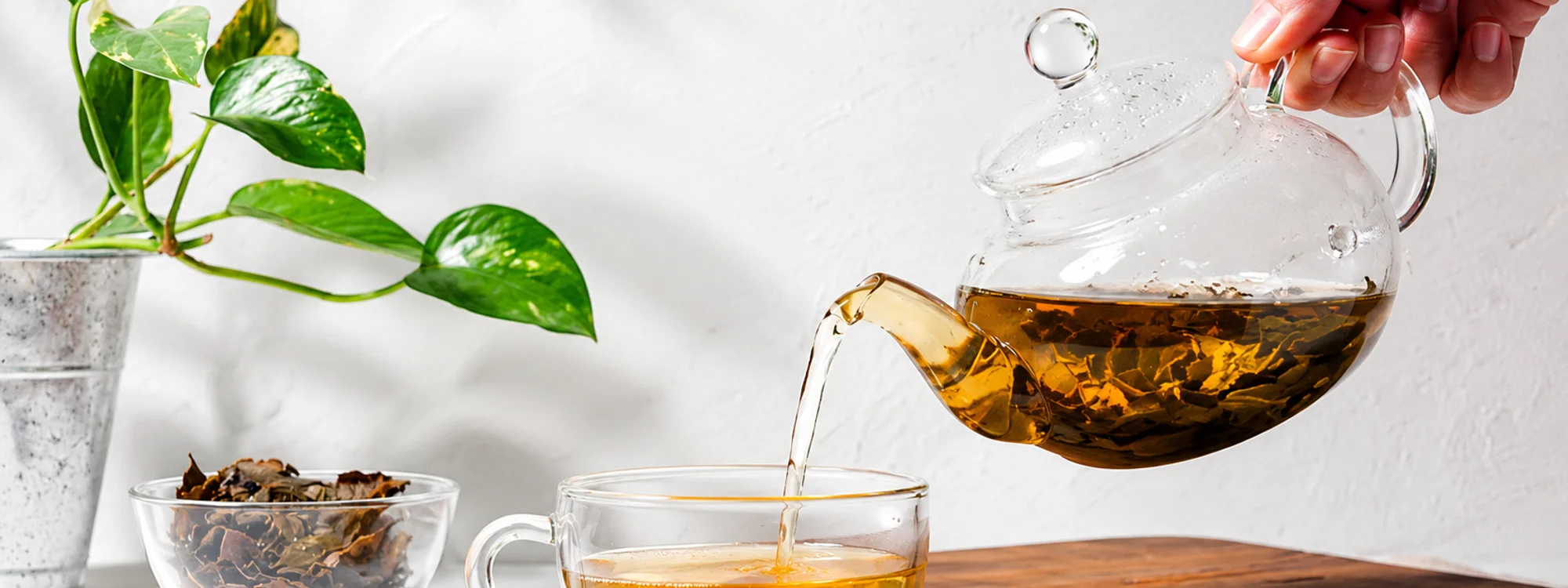 Darjeeling tea being poured from a glass teapot into a glass cup beside a bowl of dried leaves
